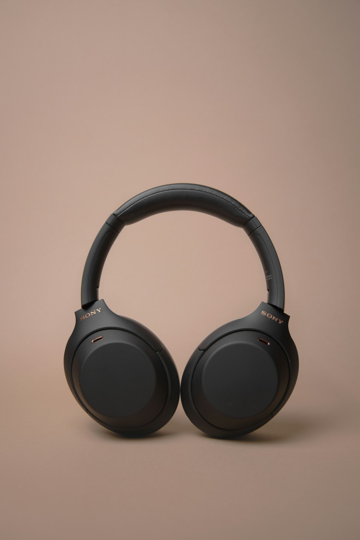 Lifestyle scene: the same headphones restaged on a warm mauve studio backdrop