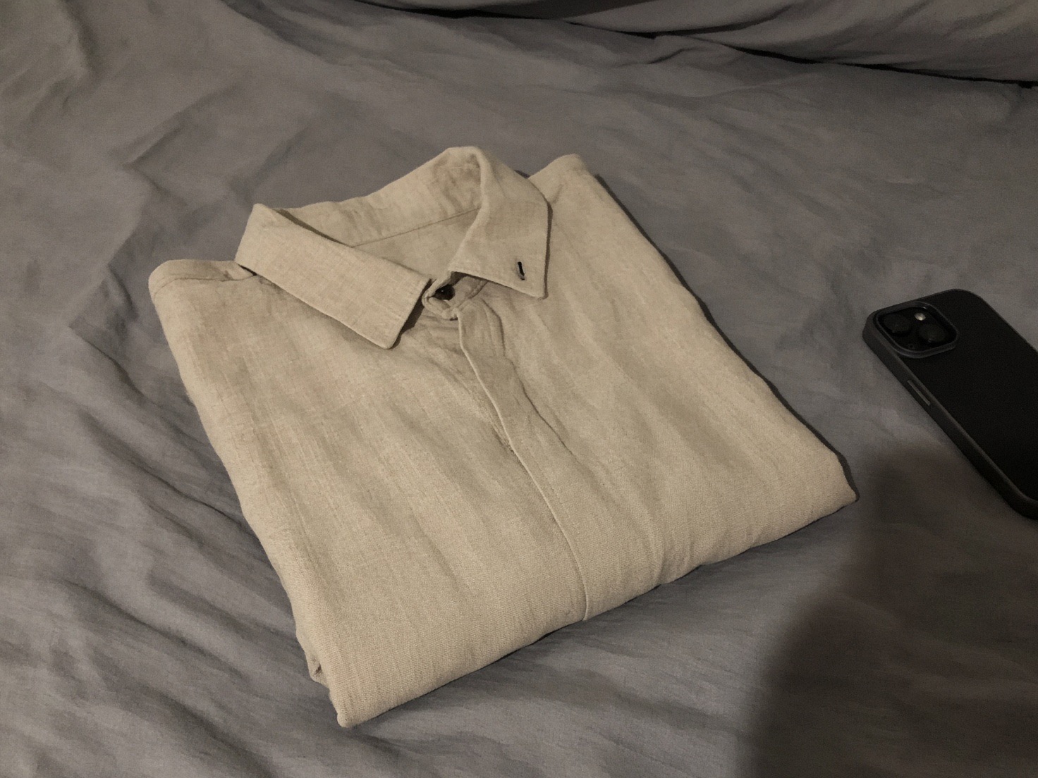 Phone photo: a folded linen shirt on an unmade bed at night