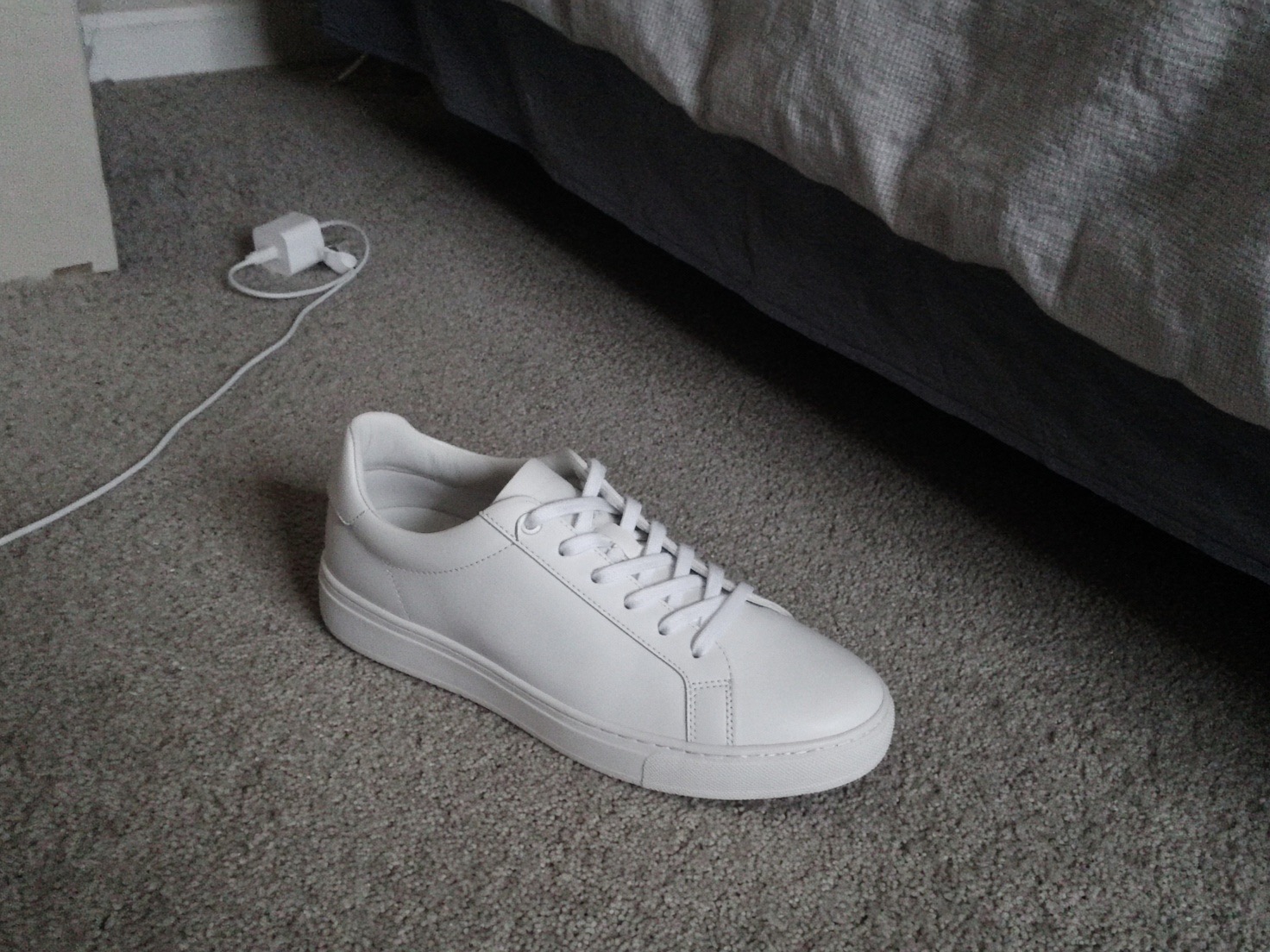 Phone photo: a white sneaker on bedroom carpet
